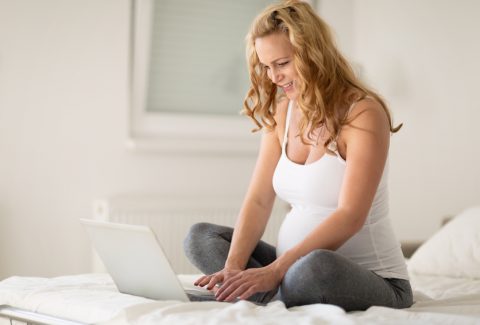 Pregnant woman using laptop on bed